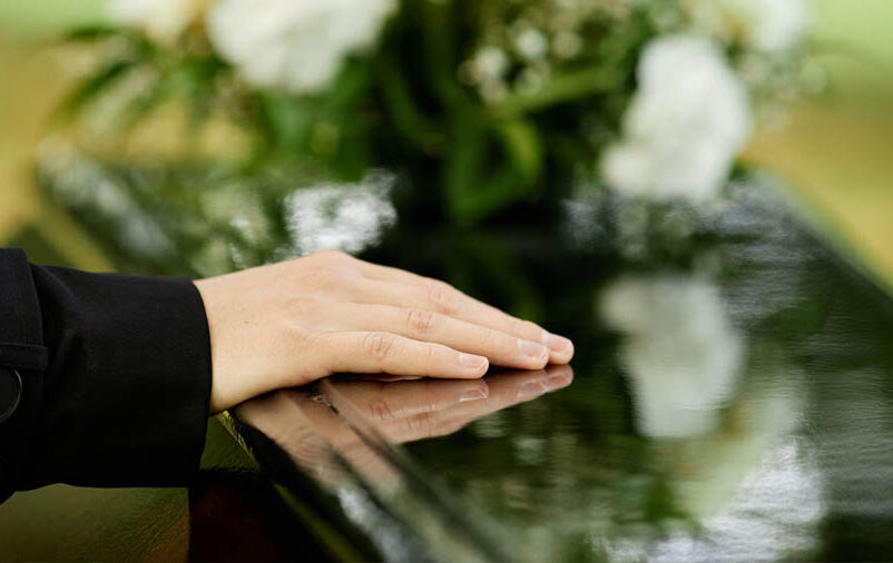 mulher com mão em cima do caixão pós funeral
