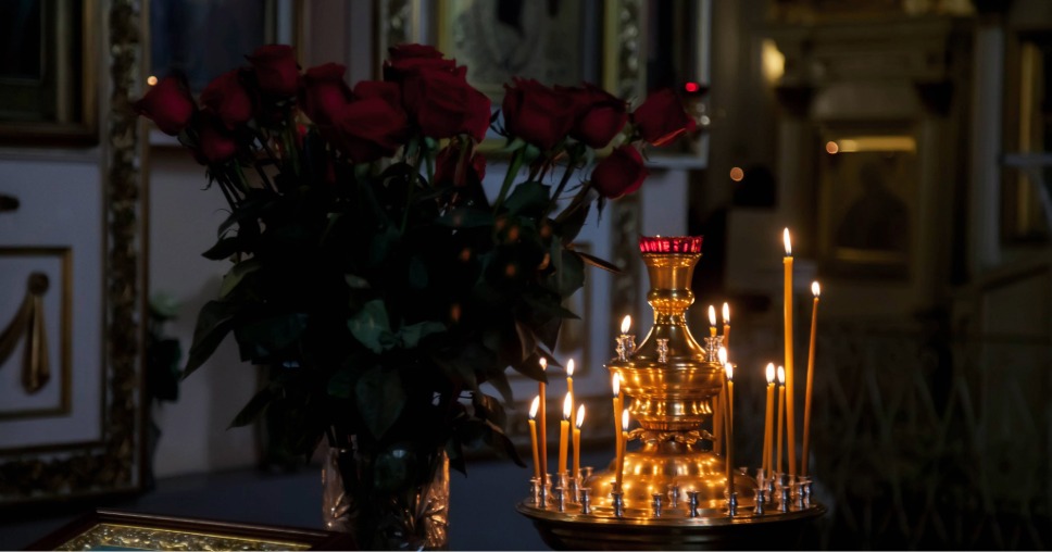 Velas finas acesas em candelabro dourado ao lado de rosas no processo de cremação.