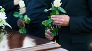 Ritos de despedida e costumes funerários pelo mundo Pessoas em trajes formais pretos segurando rosas brancas diante de urnas mortuárias no contexto de costumes funerários pelo mundo.